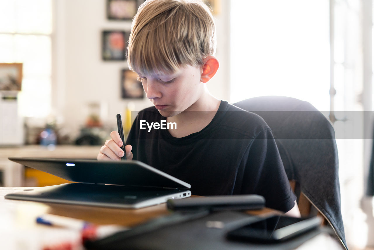 Teen working with 2in1 laptop computer at table inside home