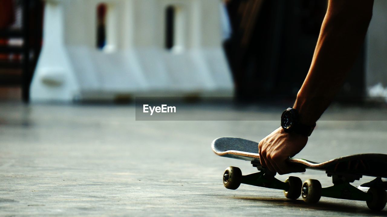 Cropped image of man holding skateboard on footpath