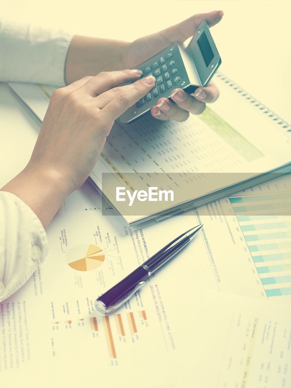 Cropped hands of businesswoman using calculator with documents at desk