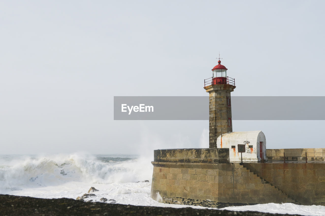 Lighthouse by sea against sky during winter