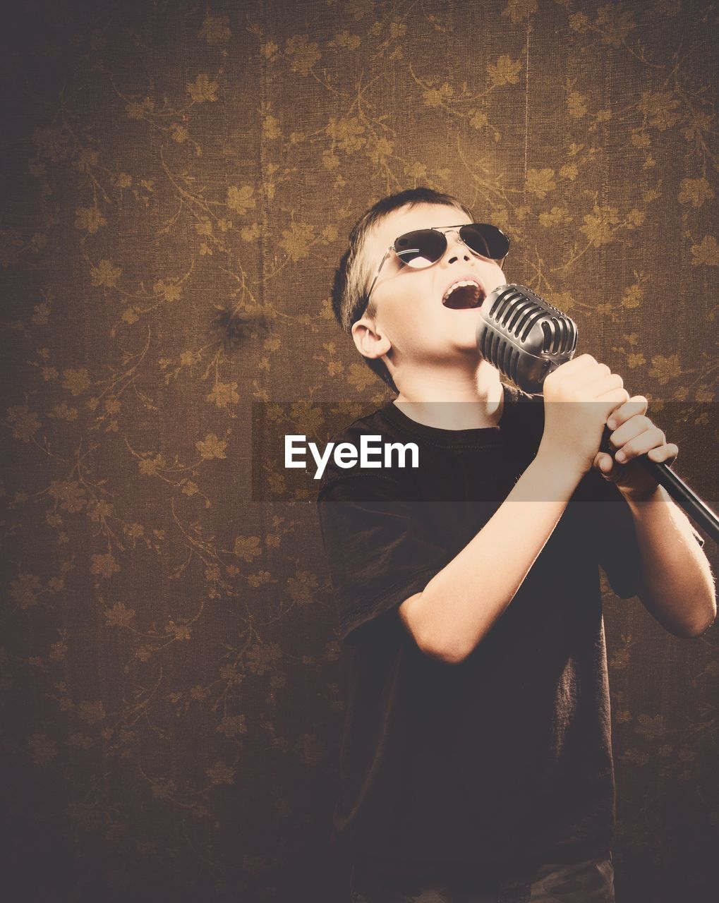 Boy wearing sunglasses while singing with microphone at home