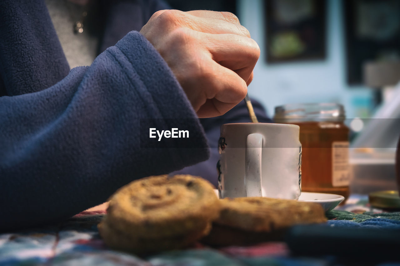 CLOSE-UP OF HAND HOLDING COFFEE CUP WITH SPOON AND TABLE