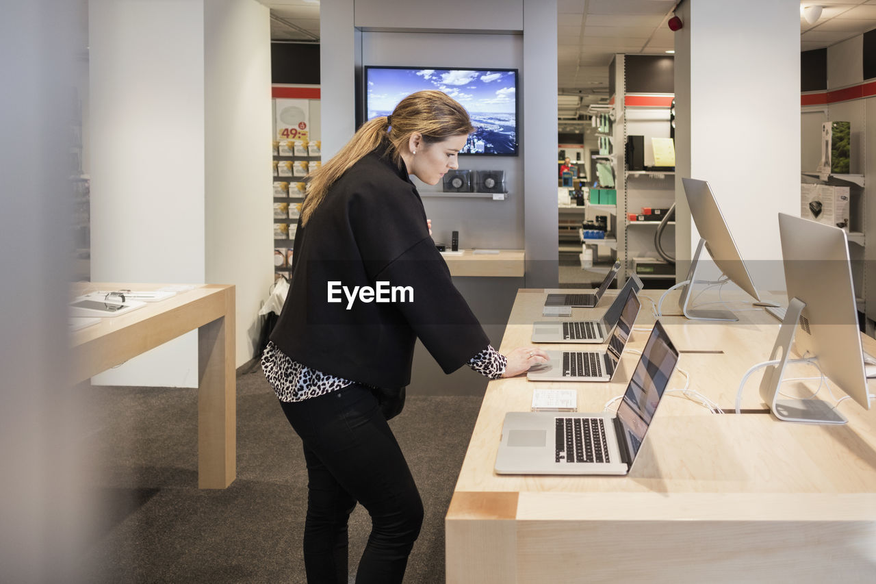 Side view of woman using laptop while standing at table in store