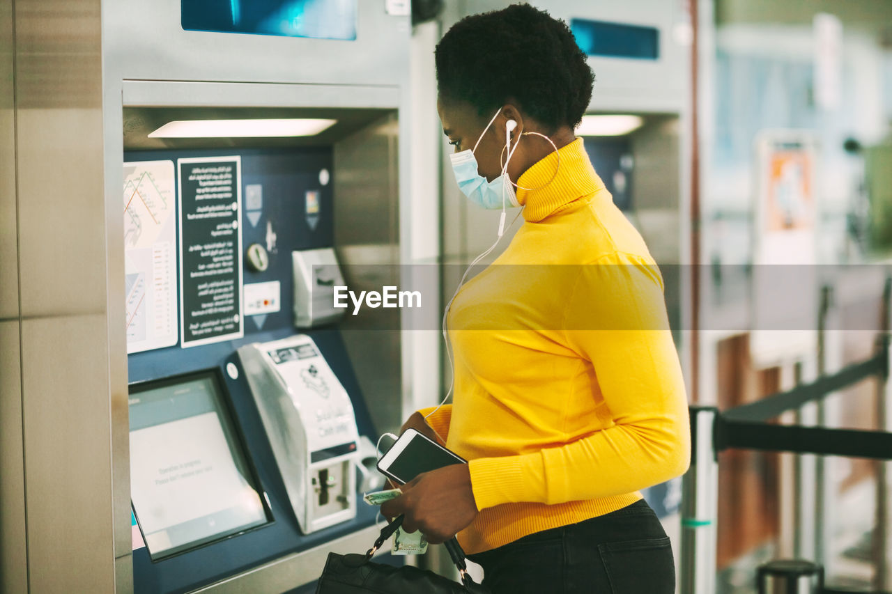 Dubai, uae, november 2020 african woman wearing a protective mask withdraws money from a bank card