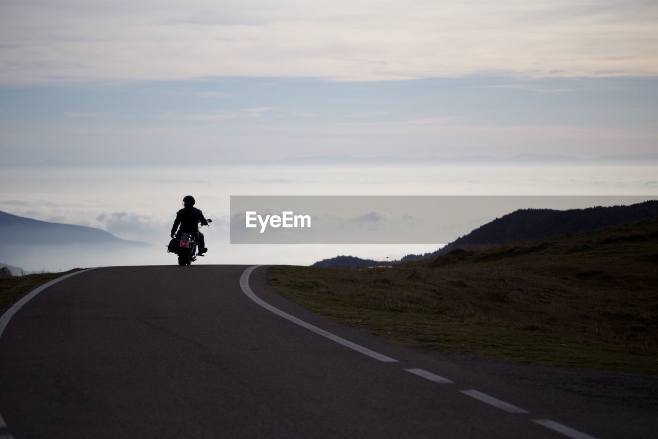 Rear view of man riding motorcycle on road against sky