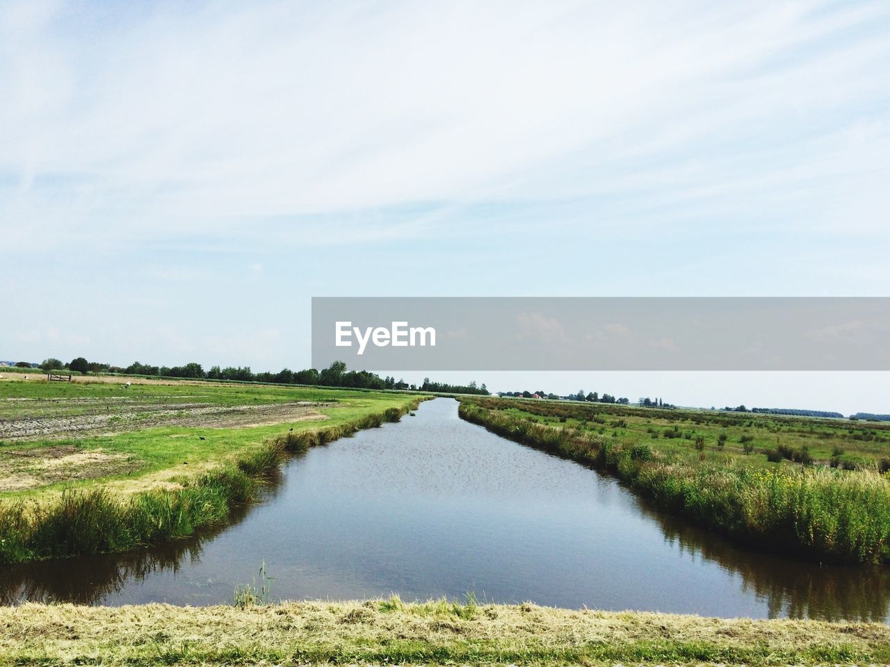 Canal amidst grassy field against sky