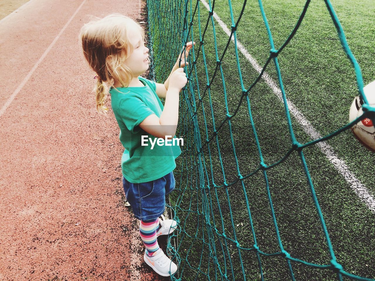 Side view of girl standing by net in playground