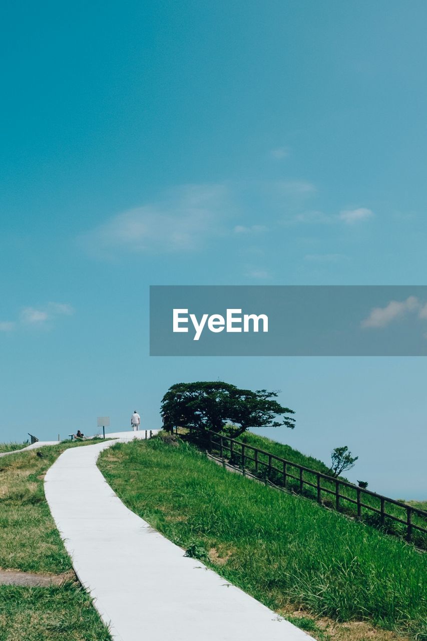 Walkway on grassy field at hill against sky