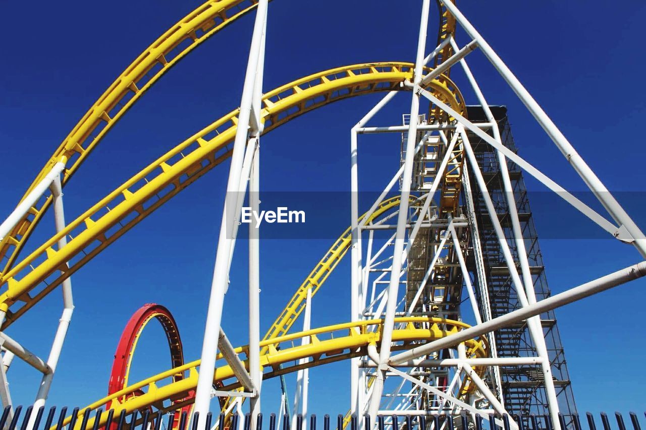 Low angle view of roller coaster against clear blue sky