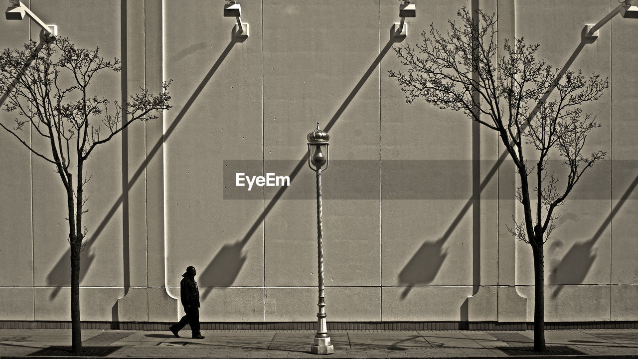 Silhouette man walking footpath by building