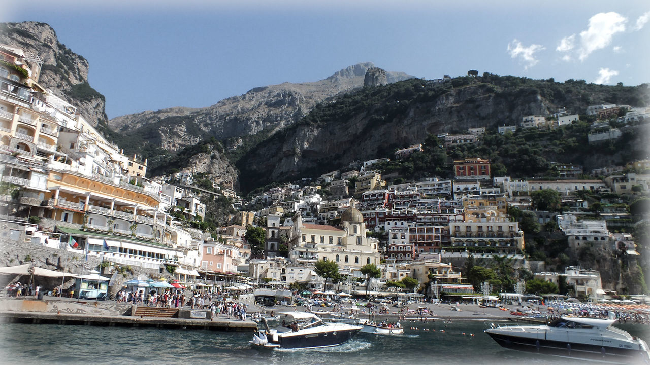 Little beach and harbor of positano italy by sea against mountain and sky