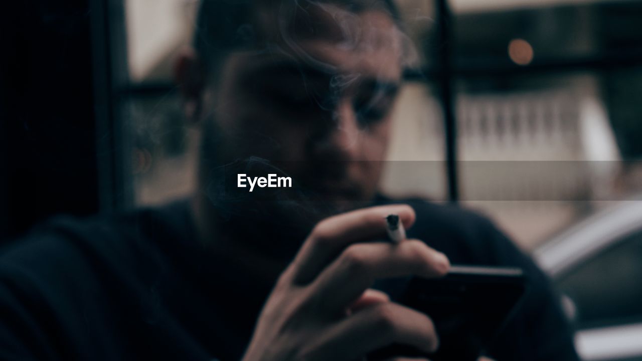 Close-up of man holding cigarette using smart phone