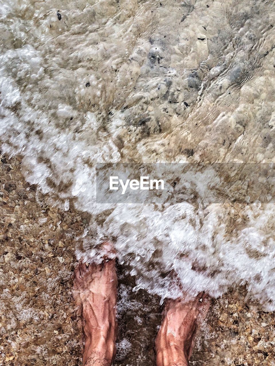 Low section of man standing at sea shore