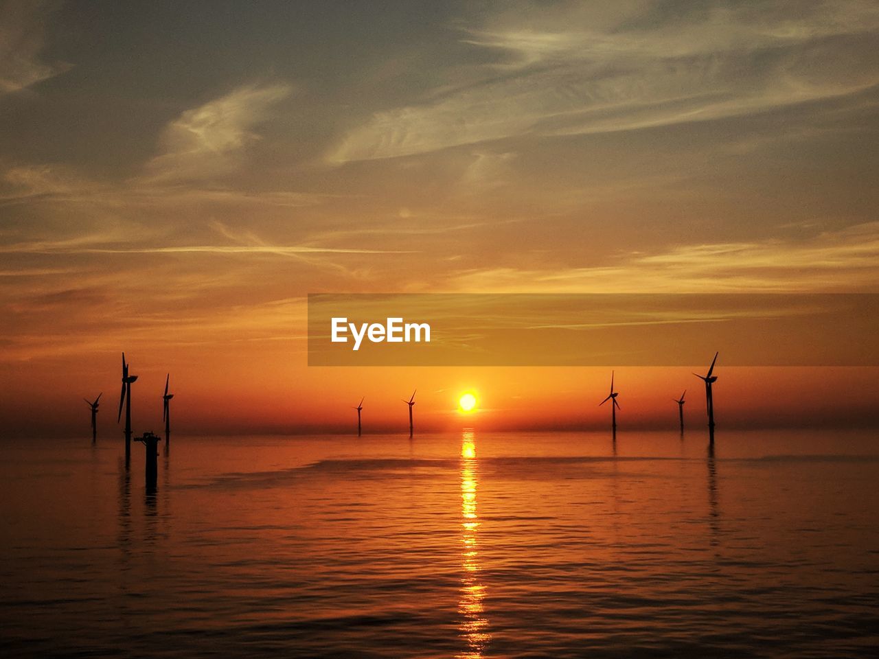 Scenic view of sea against sky during sunset featuring wind turbines