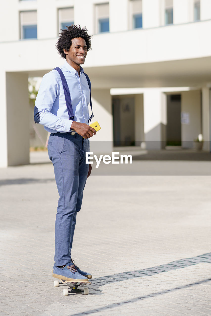 Portrait of young man standing on footpath against building