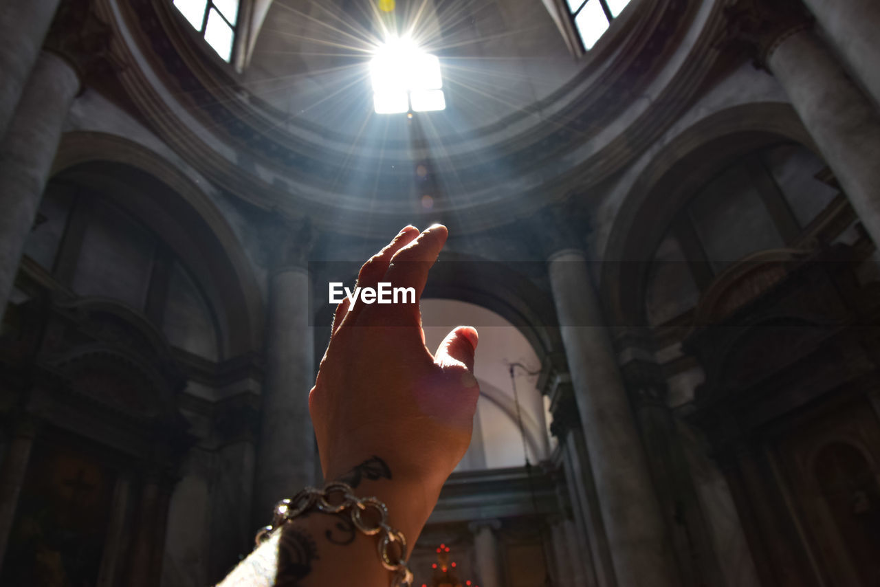 Low angle view of hand reaching sunlight in historic building