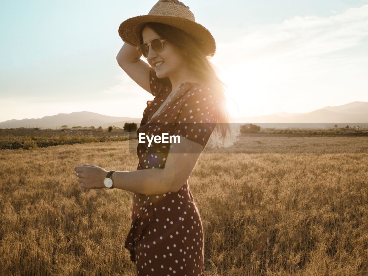 Side view of young woman standing on field against sky