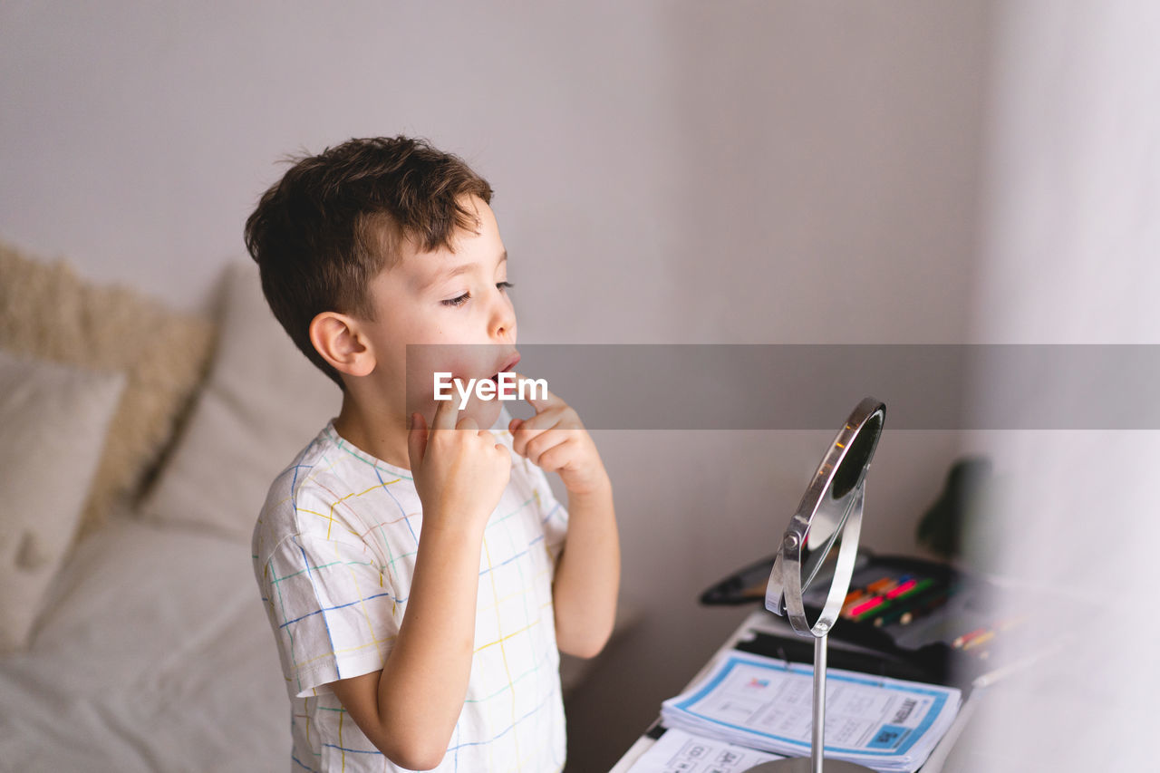 Boy pronouncing sound o looking at mirror doing an online speech therapy lesson through a laptop