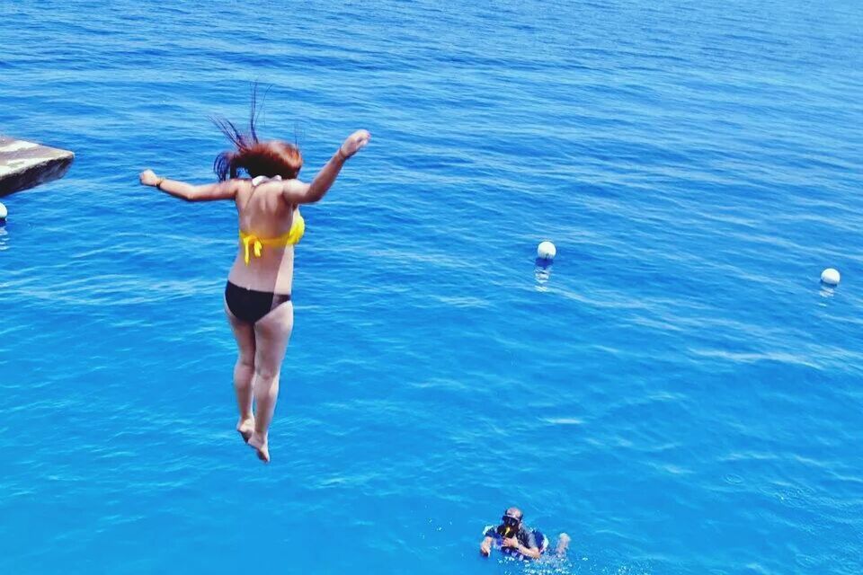 Full length rear view of woman in bikini diving in blue sea