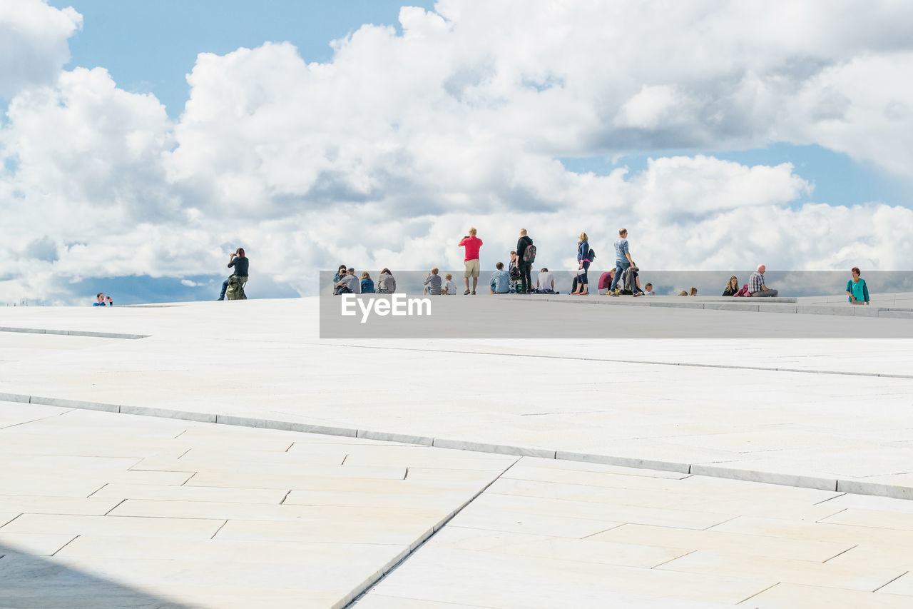 People at oslo opera house against cloudy sky