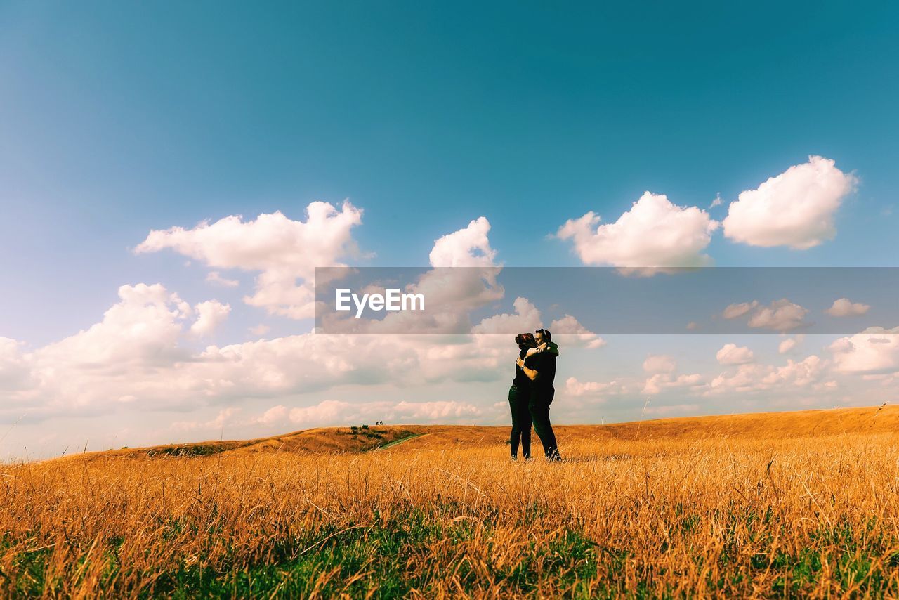 Couple kissing on grassy field against sky during sunny day