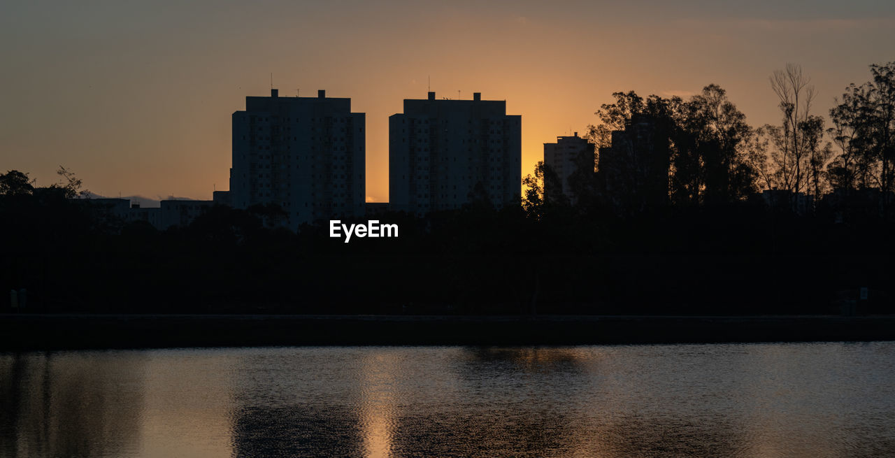 SILHOUETTE BUILDINGS BY LAKE AT SUNSET