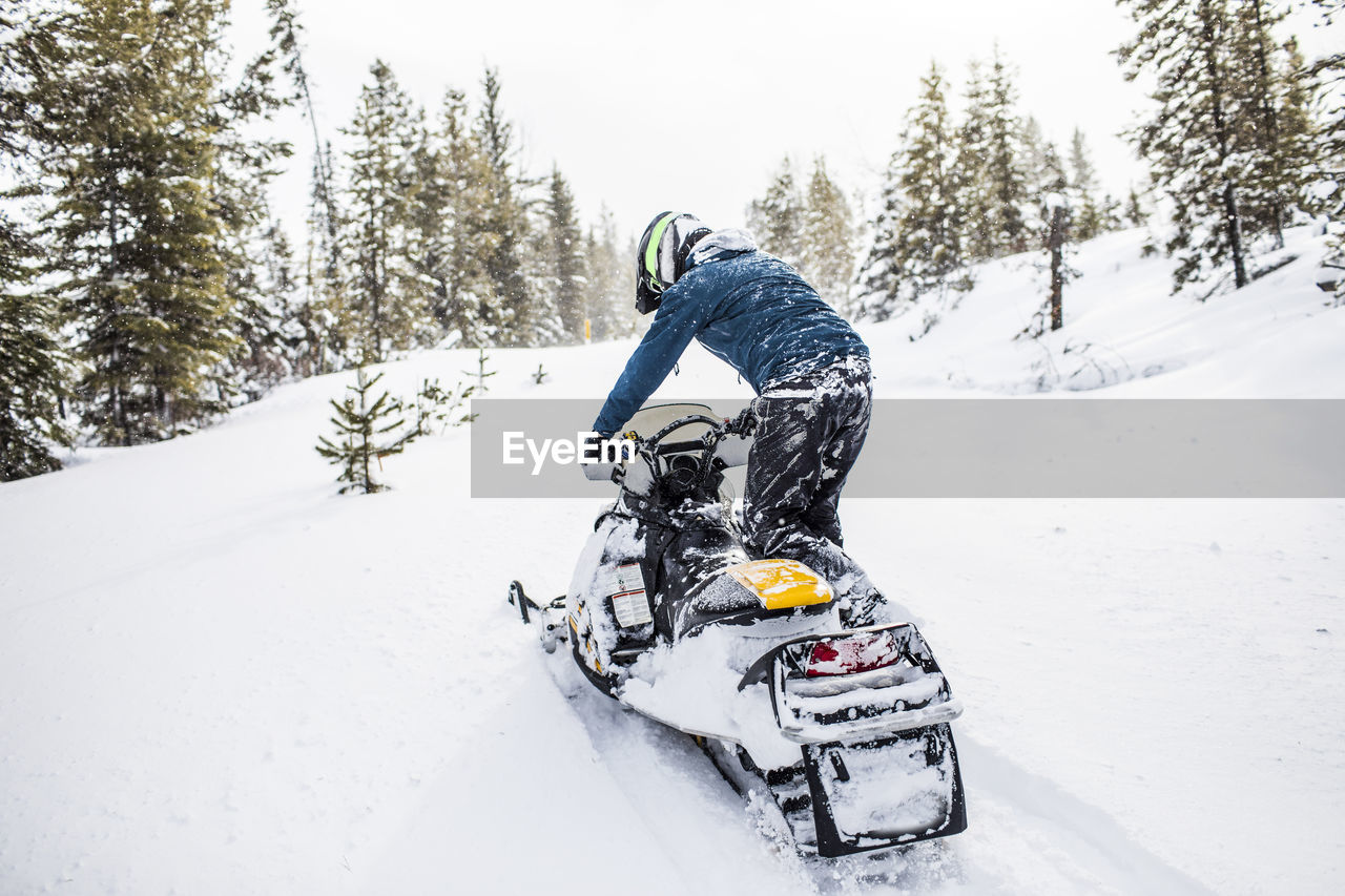 Rear view of man snowmobiling in winter weather.
