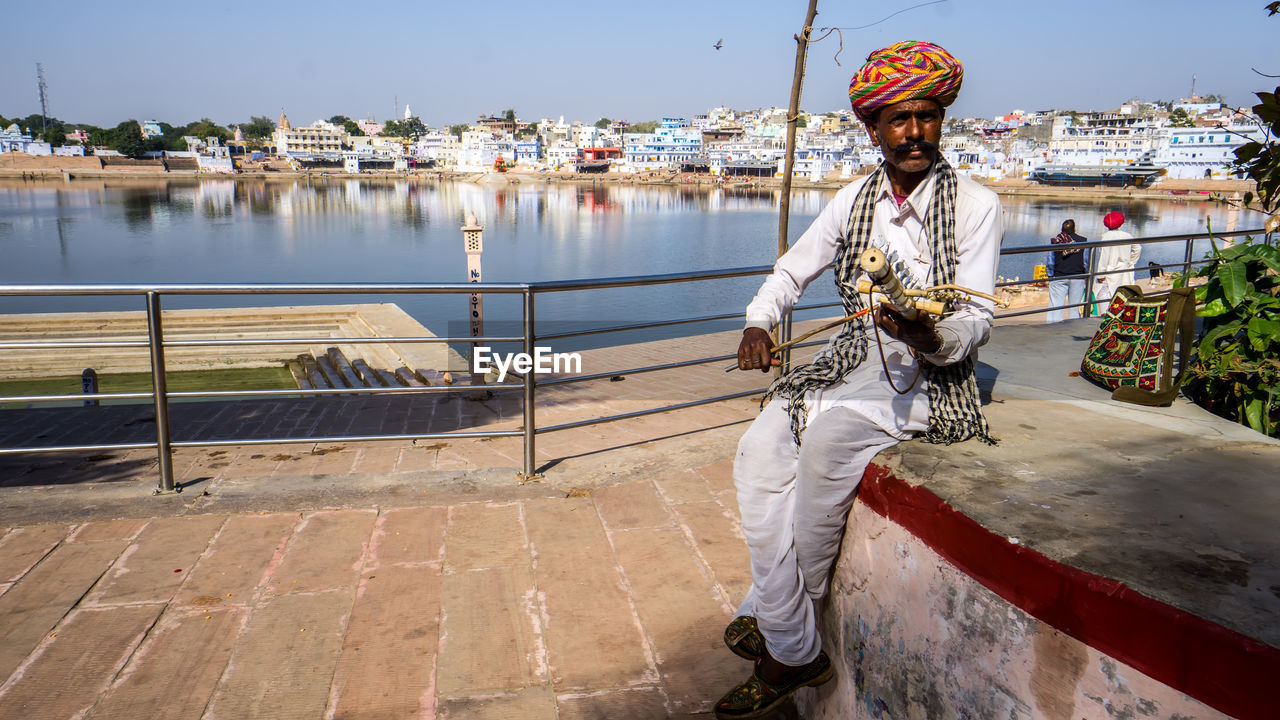 Man playing musical instrument against lake in city