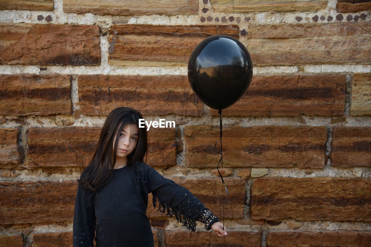Girl playing with balloon against stone wall