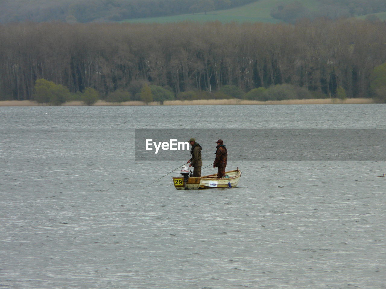 People fishing while standing on boat in lake