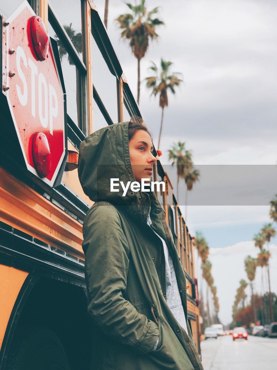 Side view of thoughtful young woman wearing jacket while standing against bus on road