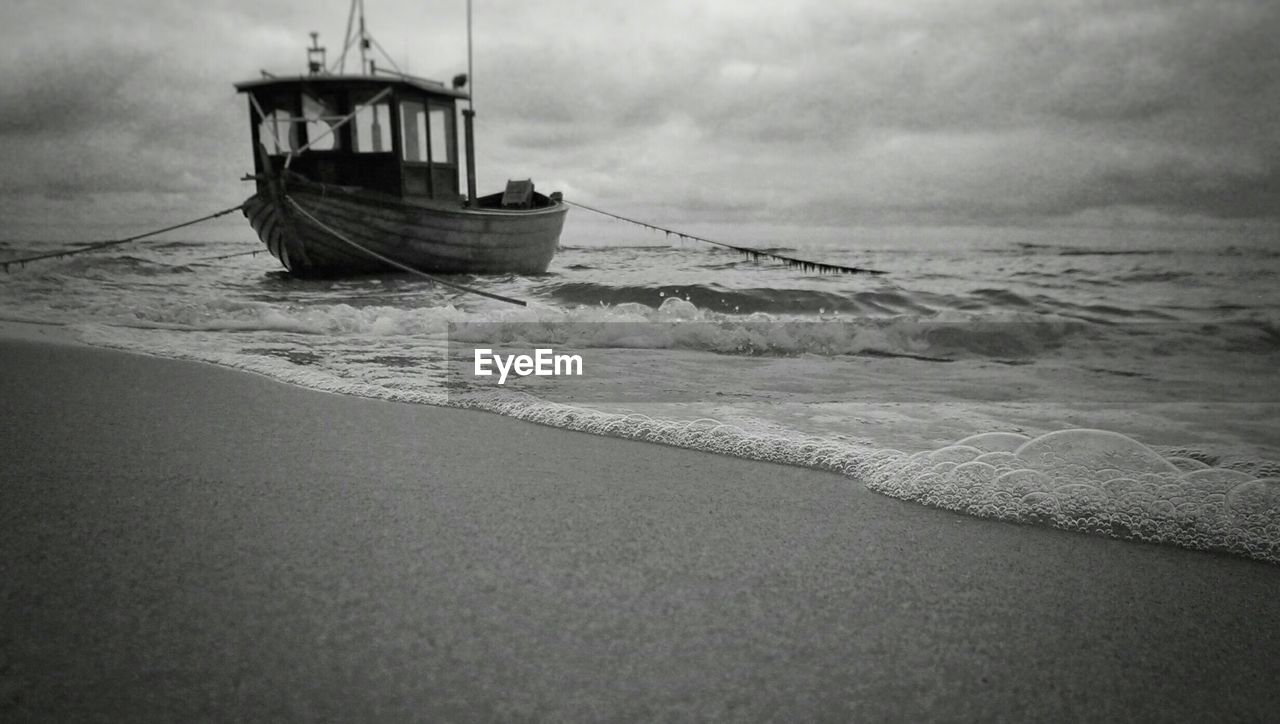 Boat moored on sea against cloudy sky