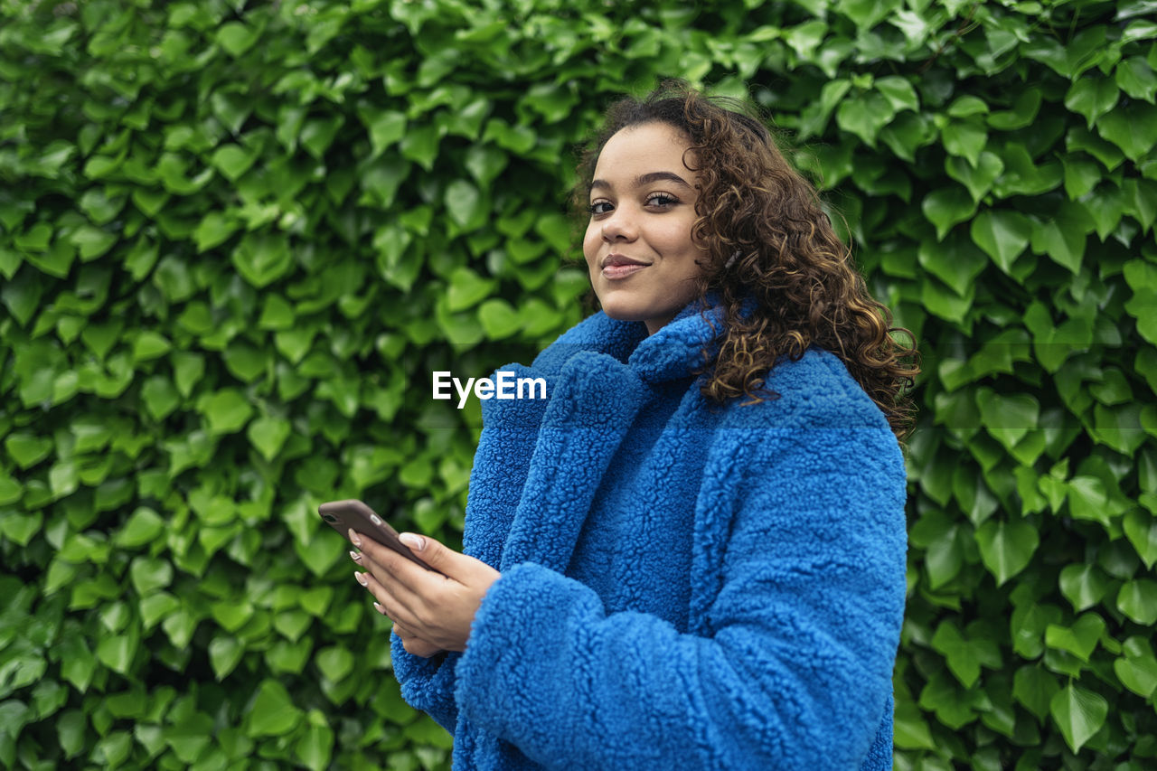 Young woman holding smart phone while standing outdoors