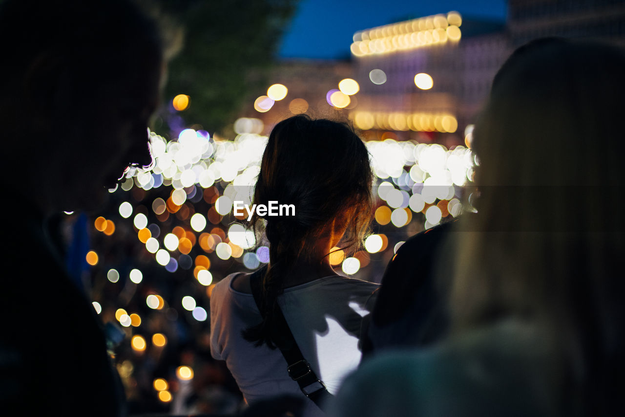 REAR VIEW OF PEOPLE ON ILLUMINATED STREET