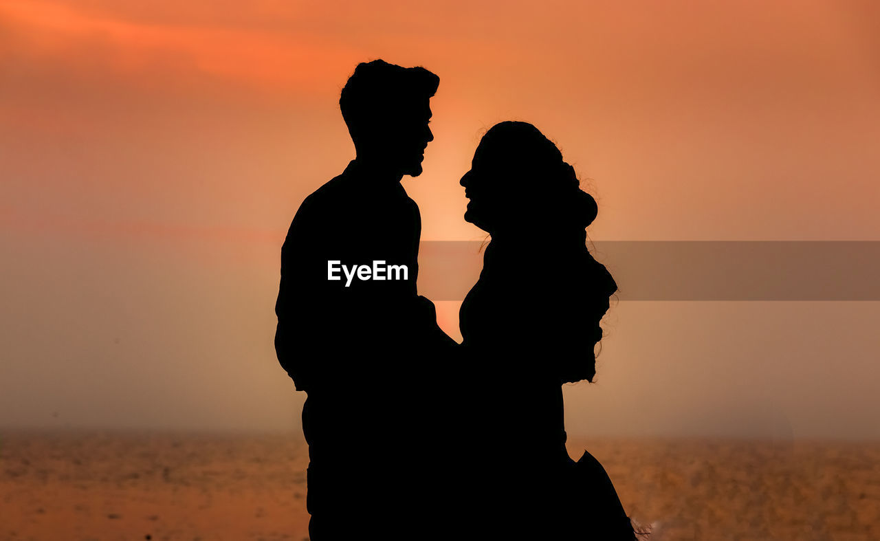 SILHOUETTE COUPLE STANDING AGAINST ORANGE SKY