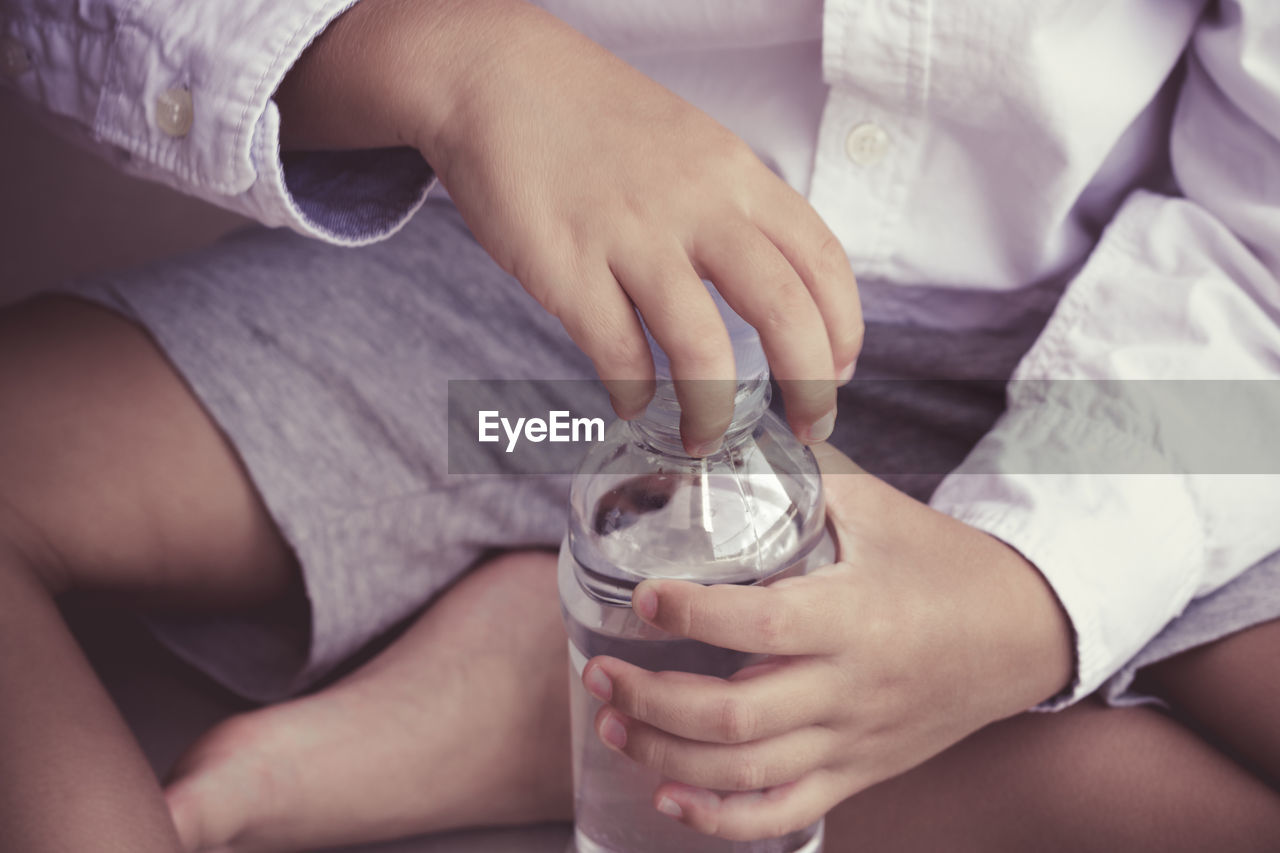 Midsection of child opening water bottle while sitting at home