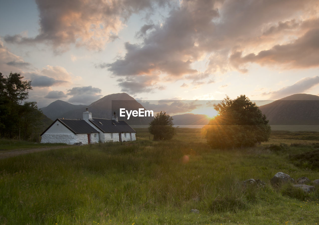 HOUSE ON FIELD AGAINST SKY AT SUNSET