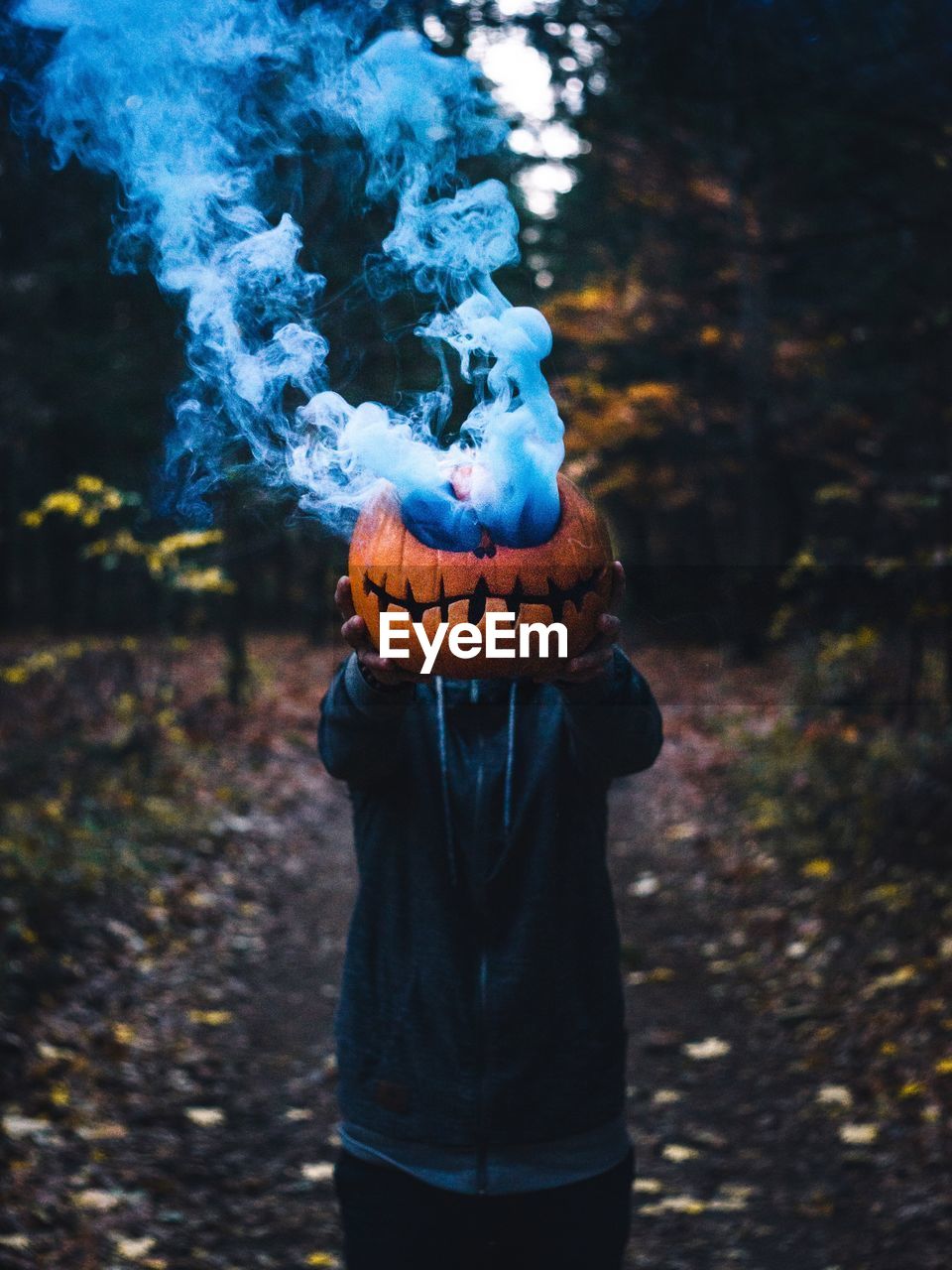 Man holding smoke emitting pumpkin while standing in forest