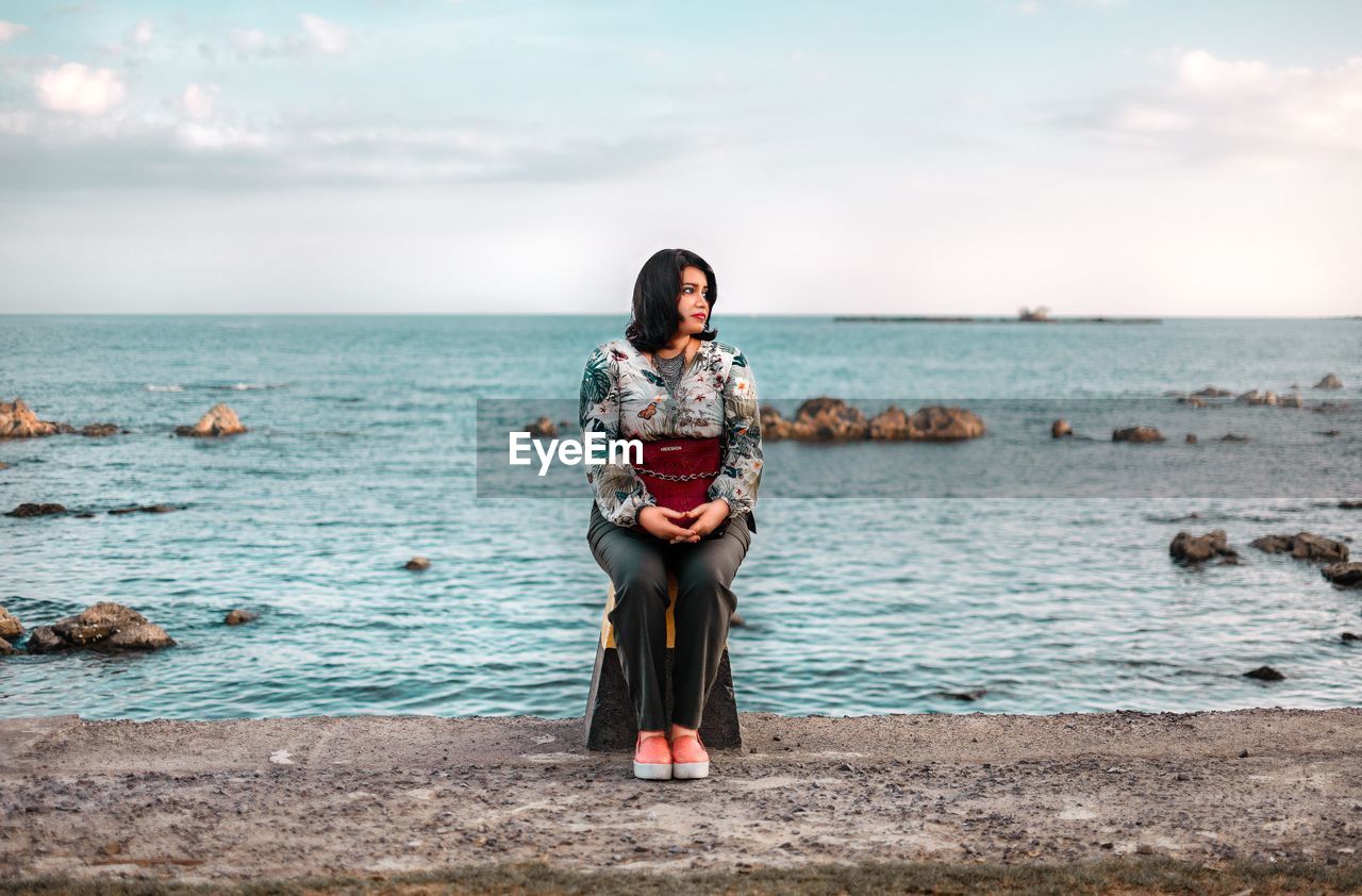 Woman sitting at beach against sky