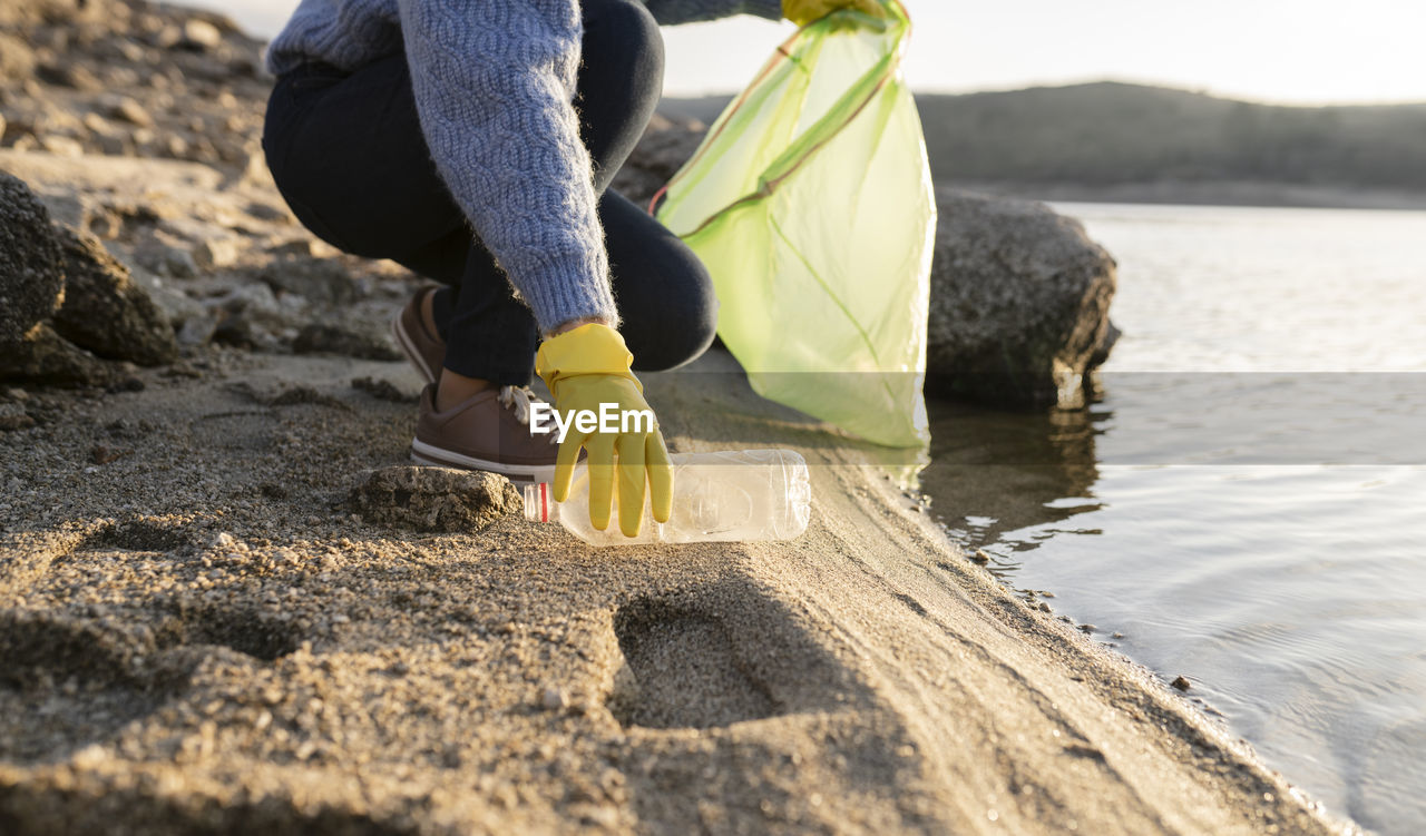 Woman picking up plastic bottle on beach by seashore