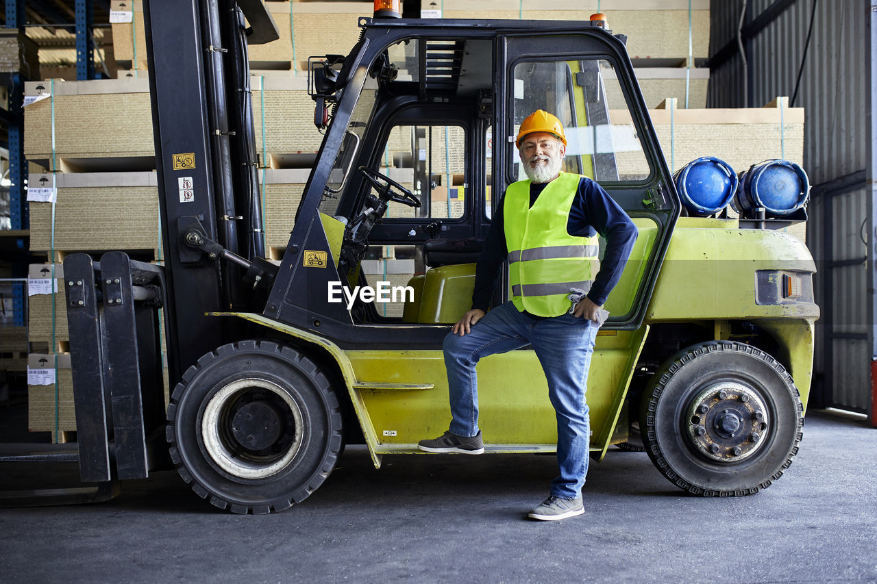 Portrait of confident mature worker at forklift in factory