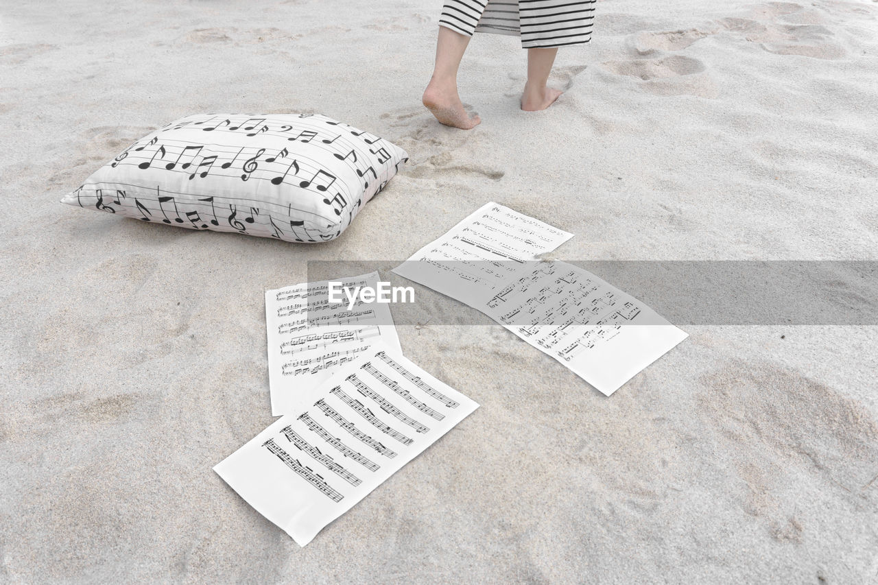 Low section of woman walking by pillow and papers on sand