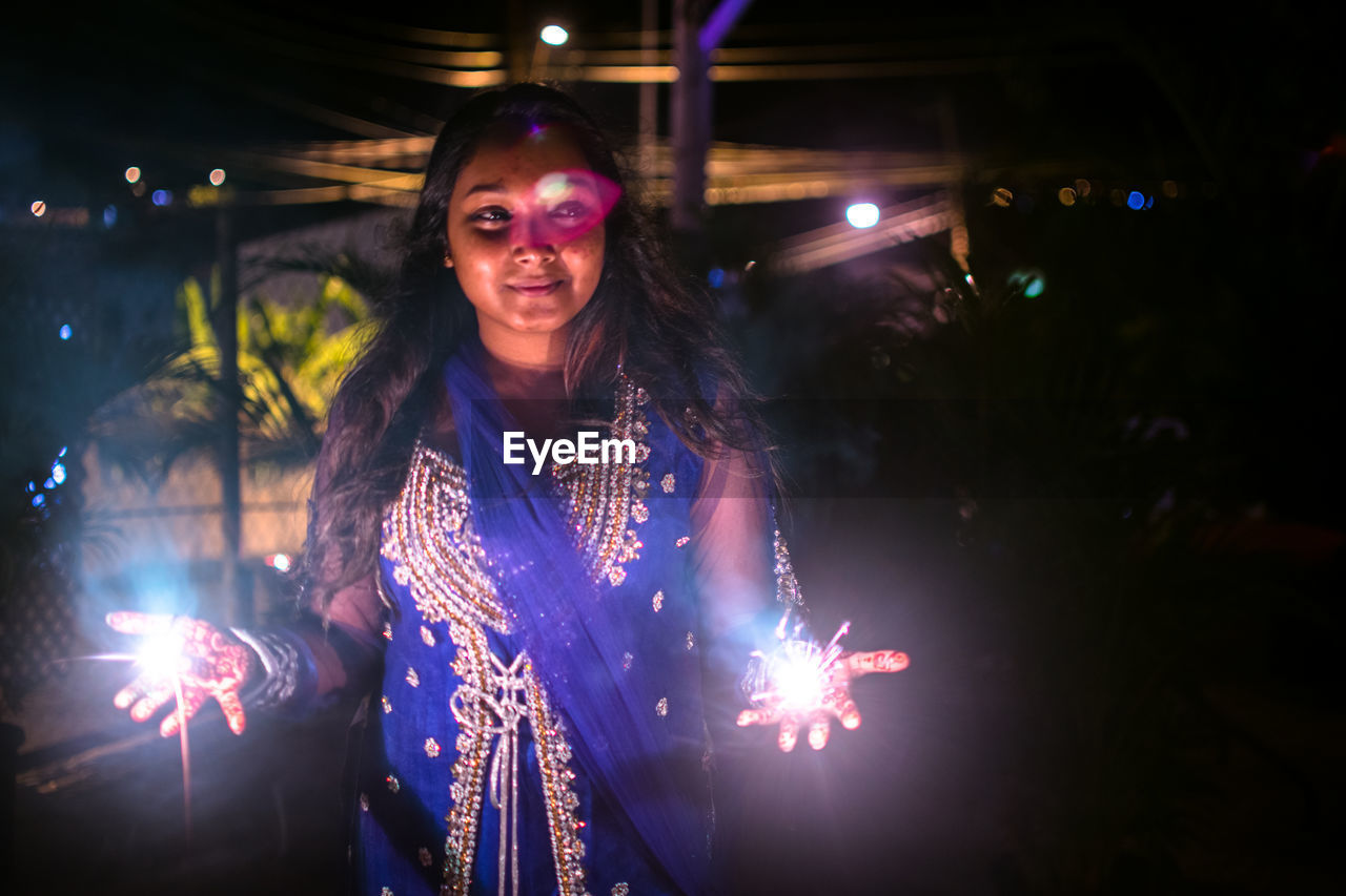 Young woman holding sparklers at night