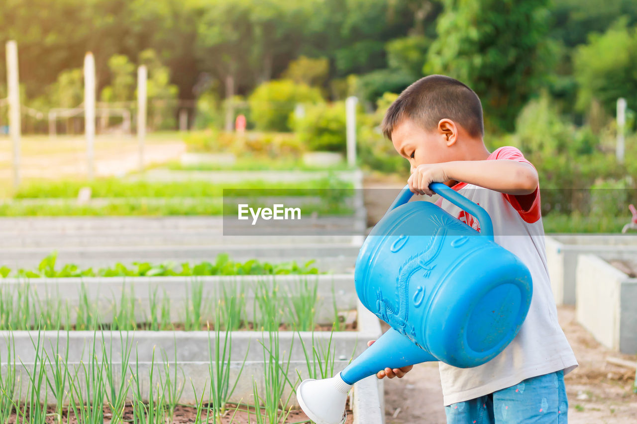 Side view of boy watering plants with can