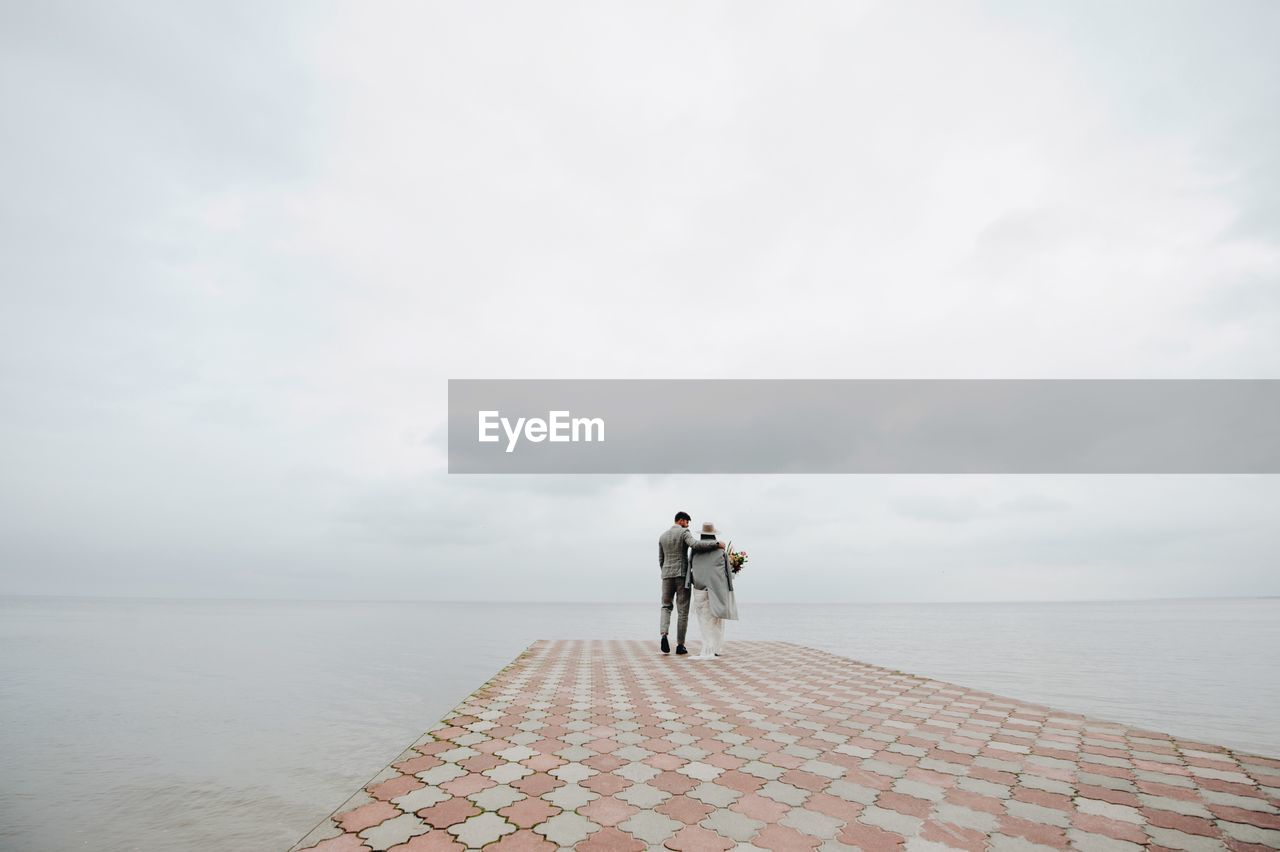 Bride and bridegroom walking on pier in sea during wedding ceremony