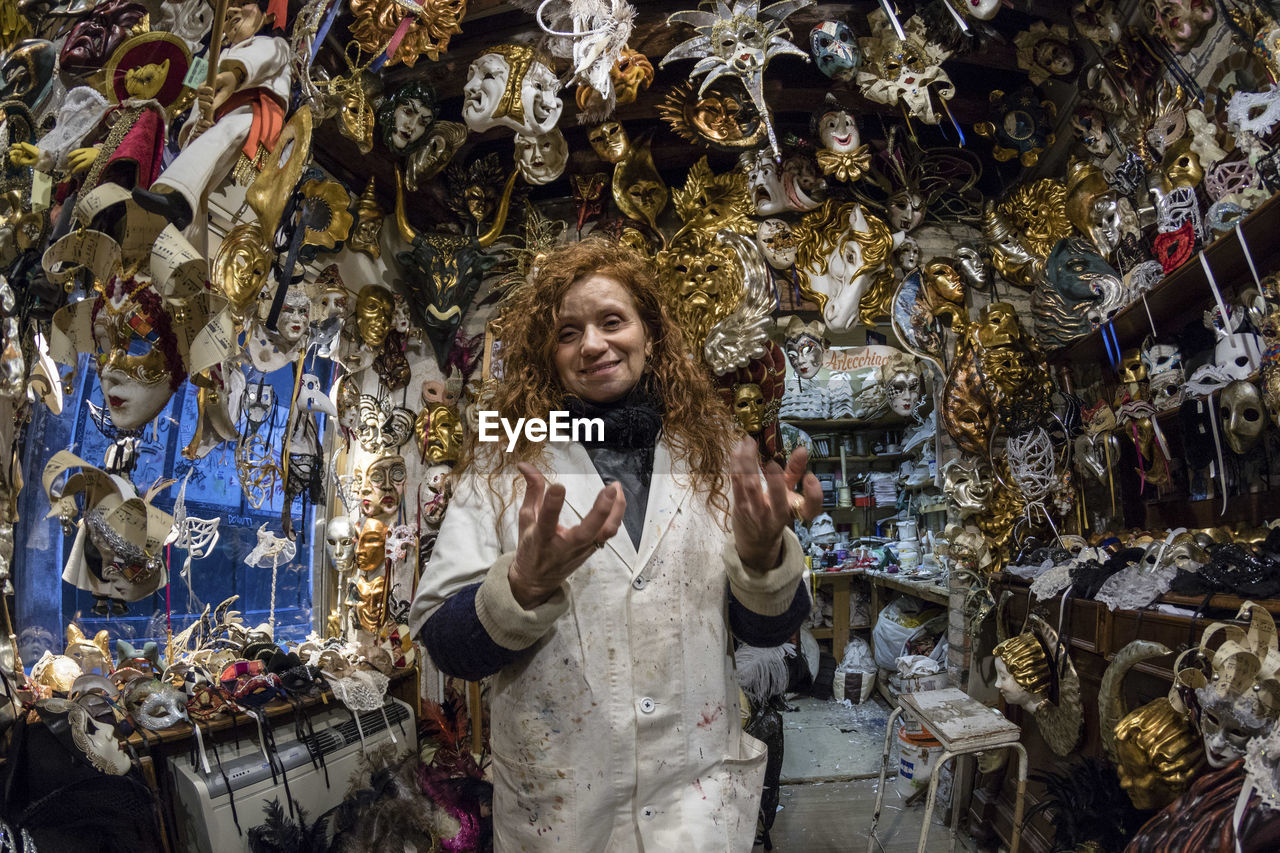Portrait of woman smiling while standing amidst masks in store