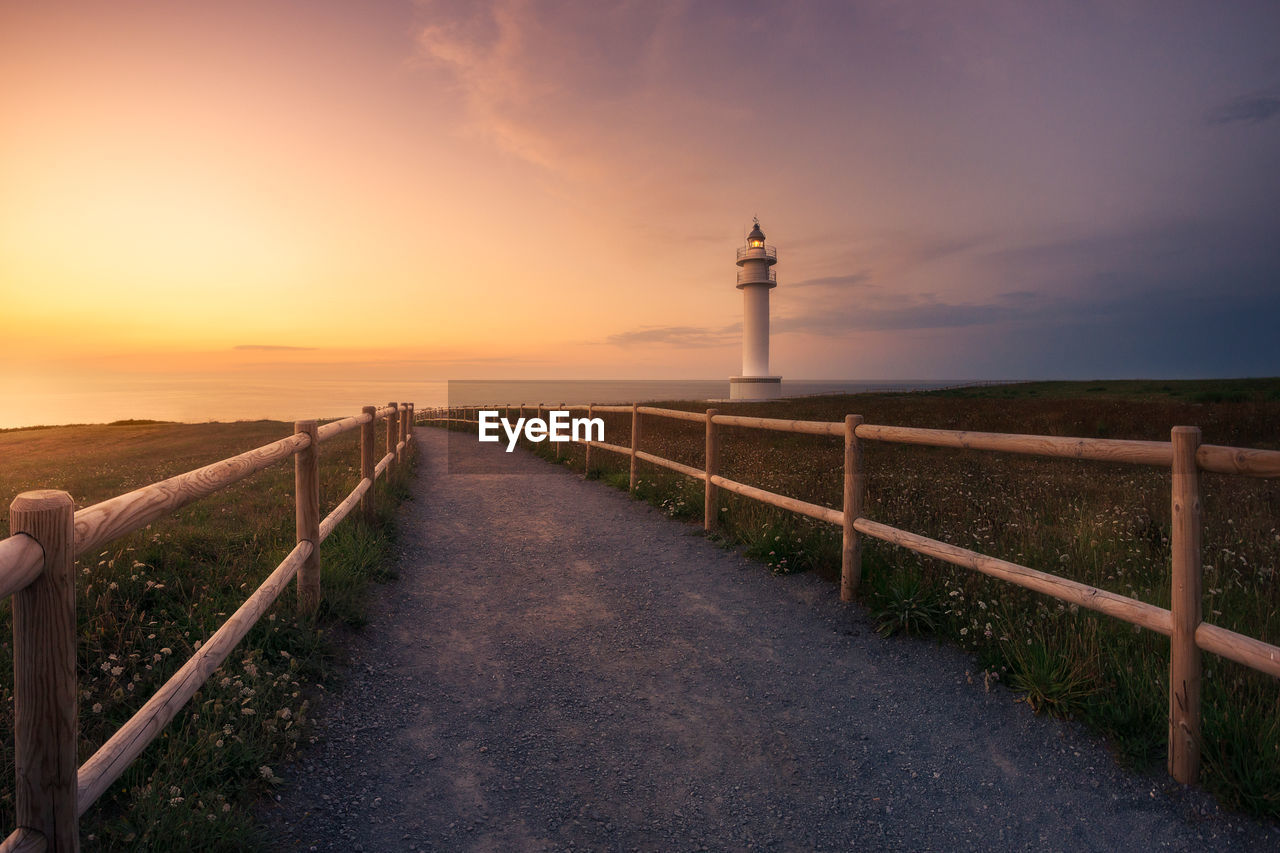 LIGHTHOUSE AMIDST LAND AGAINST SKY AT SUNSET