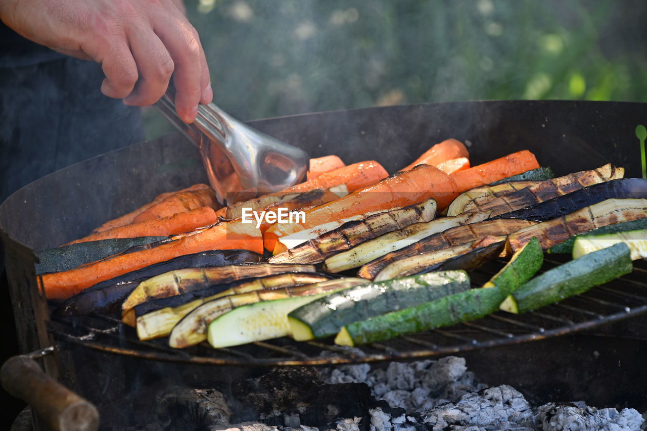 Cropped hand of man holding carrot in barbecue grill