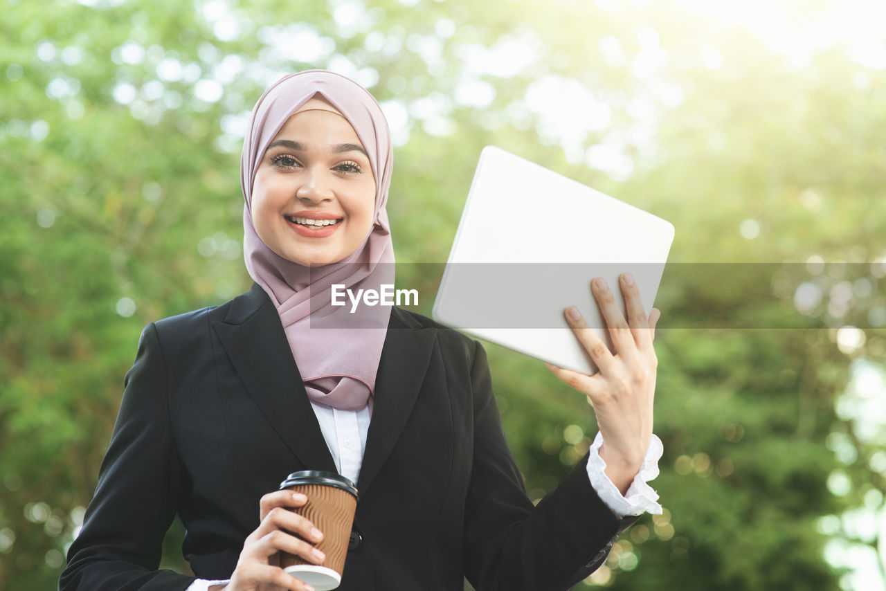 Portrait of smiling young woman in headscarf holding digital tablet