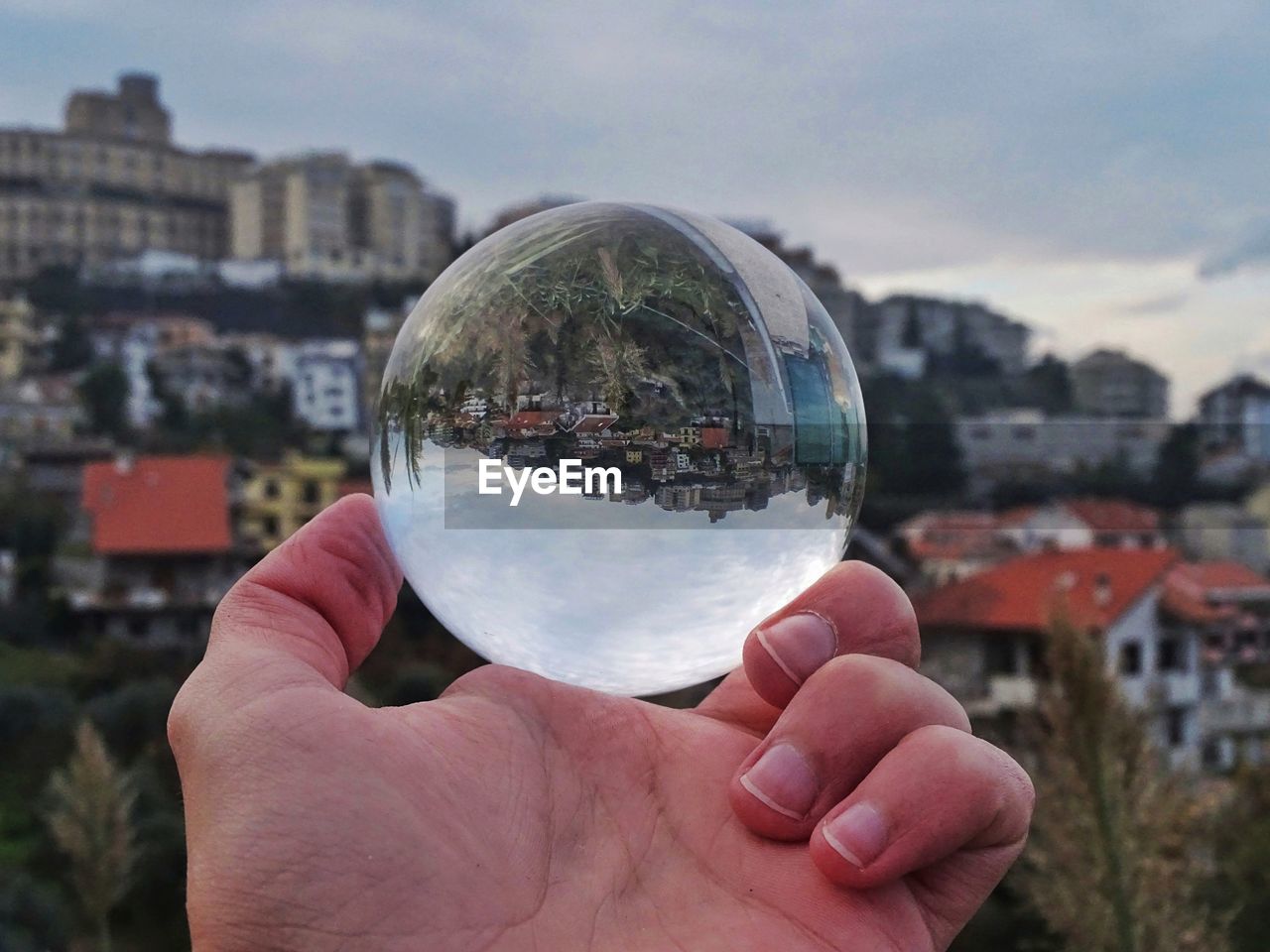 Close-up of hand holding crystal ball against cityscape